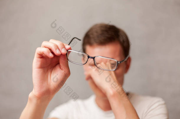 这个年轻人戴着带屈光镜片的眼镜，由于疲劳、视力和眼睛疲劳、计算机视觉<strong>综合征</strong>、近视问题、视力矫正等原因擦拭眼睛
