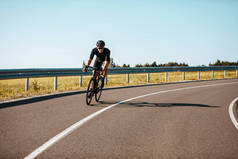 在农村，穿着运动服的积极的成熟男子骑着自行车走在铺好的路上。戴黑色头盔和眼镜的经验丰富的骑单车者定期在户外训练.