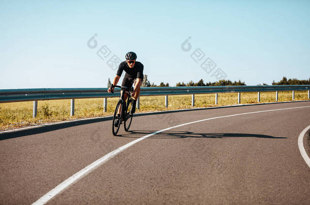 在农村，穿着<strong>运动服</strong>的积极的成熟男子骑着自行车走在铺好的路上。戴黑色头盔和眼镜的经验丰富的骑单车者定期在户外训练.
