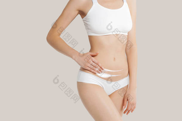 身穿内衣裤的瘦<strong>小年</strong>轻女子在米色背景的腹部涂上奶油。皮肤和身体护理