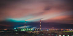 火力发电厂的照明管，冒出浓烟。五彩斑斓的天空，灯火通明。污染。夜间工业城市景观.