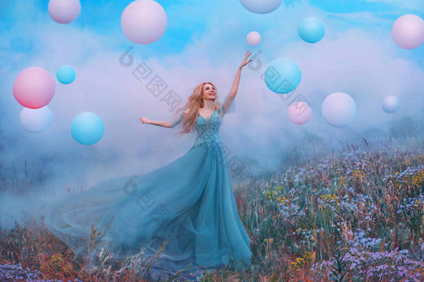 年轻快乐的金发女人举起了手。幻想公主跳跃触及粉色气球。长长的蓝色郁金香裙在风中飘扬。白云、雾、烟五彩斑斓的草甸