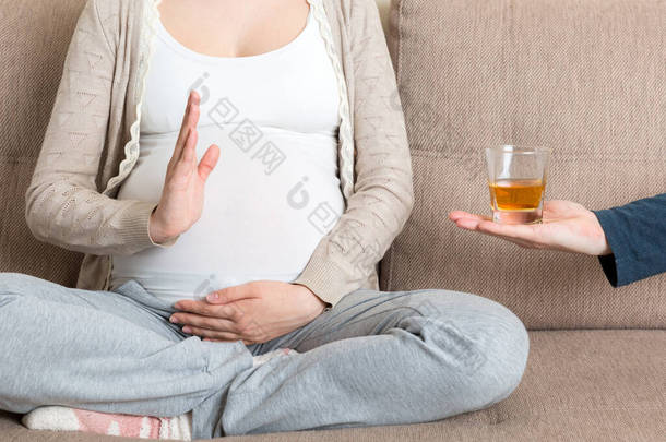 靠近坐在沙发上的孕妇拒绝喝威士忌，并对着杯子做停止手势。<strong>怀孕</strong>期间不饮酒.