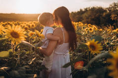 妈妈和儿子拥抱,欢笑,在向日葵地里玩耍.快乐的家庭时光在户外度过。母亲节.