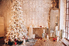 温馨舒适的夜晚豪华圣诞房室内设计，装饰着金灯的圣诞树献上礼物、蜡烛、镜子花环照明壁炉。假日客厅。新年假期的概念