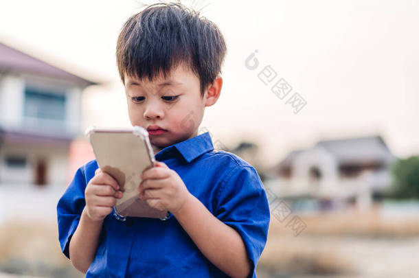 使用数码智能手机放松的可爱的亚洲小男孩的肖像。年轻的亚洲小孩看屏幕打字信息和在网上或社交媒体上玩游戏 
