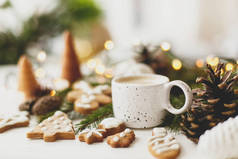 圣诞姜饼饼干，白杯咖啡，松果，白色木制桌子上的暖灯。你好，冬天，舒适的情绪画面，有选择的焦点