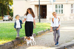快乐的家庭带着狗在城市街道上散步。时尚的母亲和孩子们在户外和他们的狗玩得很开心。小狗杰克 · 鲁塞尔，小狗和主人在散步。家庭、宠物和生活方式。快乐的家庭