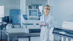 女研究科学家带着装有样品的试管盘走过实验室。背景下的创新设备实验室工作人员.