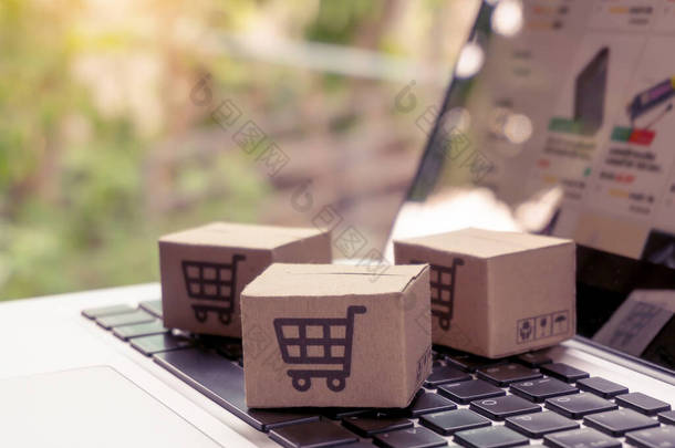 网上购物-在笔记本电脑键盘上印有购物车标志的纸箱或包裹。 网上购物服务，提供上门派递服务.