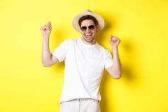 旅游、旅行和度假概念。快乐的高加索人跳舞，度假愉快，戴着墨镜，戴着草帽，站在黄色的背景下