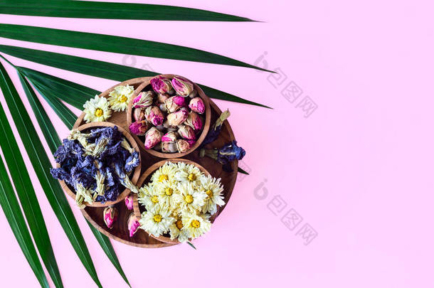 用棕榈叶隔离在粉红色背景下的木制碗中分发干茶。各种草本健康的异国情调的热带<strong>红茶玫瑰</strong>、蝶豆（蓝茶） 、菊花。带有版权空间的顶级视图.