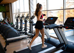 穿着运动服的漂亮瘦小的女运动员在体育馆里做健身锻炼。运动员在跑步机上跑步.健康的生活方式动机
