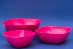 蓝色背景上的一组粉色盘子。厨房用的塑料器皿.顶部视图。简约主义风格。复制，空的文字空间.
