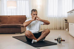 老年病人，流鼻涕坐在黑色瑜伽垫上。待在家里的概念。锻炼或健身后,人都会打喷嚏.生病时在家练习运动。用运动器材做运动.