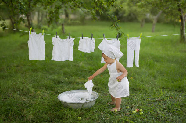一个孩子在地下室里愉快地洗衣服。从洗衣服中喷出水和泡沫。穿着白色衣服的女孩把湿衣服挂起来晾干.在一个老式的洗脸盆里洗.