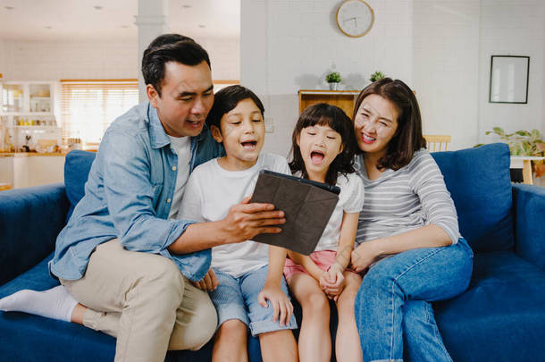 快乐快乐的亚洲家庭爸爸，妈妈和孩子们玩得开心，在家里的沙发上使用数码平板电视。自我隔离、待在家里、与他人保持距离、<strong>检疫</strong>以预防结肠炎.