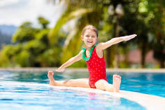 在游泳池里的孩子有孩子的家庭的热带假期。小女孩穿着红色草莓泳衣在异国情调的海岛度假胜地的室外游泳池里玩耍。为孩子们提供水和游泳的乐趣