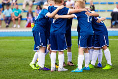 足球队队员成群结队.孩子们在赛前做运动和激励运动。儿童在蓝色足球泽西运动服。快乐校园小朋友