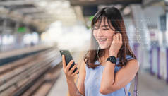 亚洲妇女通过智能手机进行面部识别，并在火车站平台上收听音乐、生物鉴别和人工智能概念