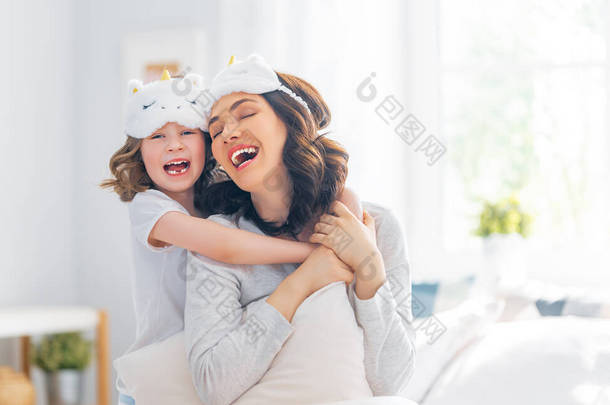 一个漂亮的女孩和她的母亲享受着阳光灿烂的早晨。在家里玩得很开心孩子从睡梦中醒来。家人在卧室的床上玩耍.