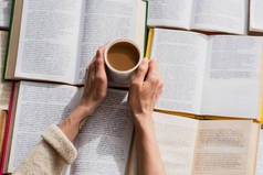 在打开的书本前，妇女端着一杯咖啡的半影 