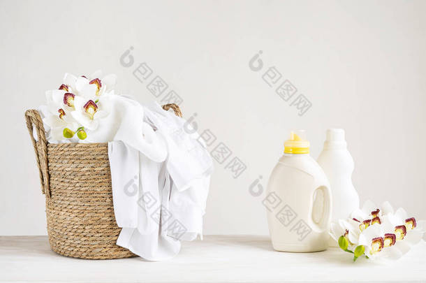柳条篮，白色亚麻布，洗涤剂和织物柔软剂在白色桌子上，兰花。设有复印间的模拟洗衣店日.