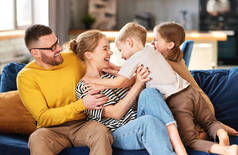 快乐的家庭，年轻的父母和两个可爱的兴奋的孩子在一起玩乐、拥抱和玩耍，同时在家里的沙发上放松。妈妈、爸爸和孩子们享受闲暇时光