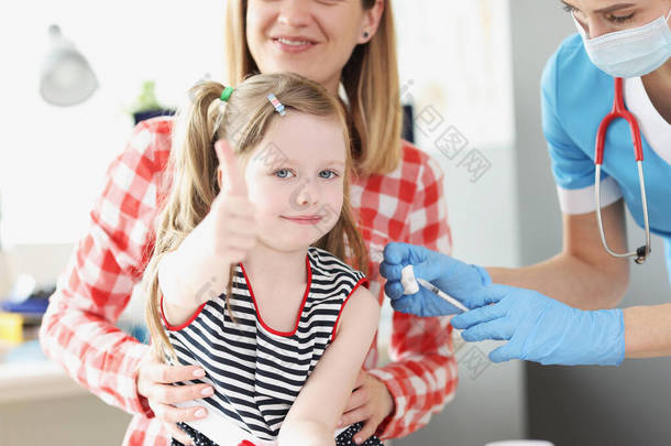 小女孩竖起大拇指，医生在医院给她的肩膀注射疫苗