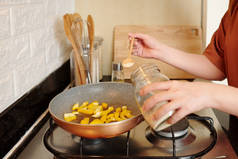 妇女在为家人做饭时，将米饭和胡椒粉放在油锅里的双手