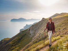 女徒步旅行者在土路上行走。徒步旅行时使用远足杆子的妇女。欣赏阳光普照的大海。山区和沿海旅行、自由和积极的生活方式