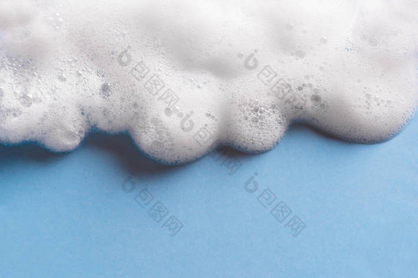 面部清洁慕斯样品。蓝色背景的白色清洁剂泡沫泡沫，复制空间。肥皂、淋浴露、洗发水泡沫质感特写.