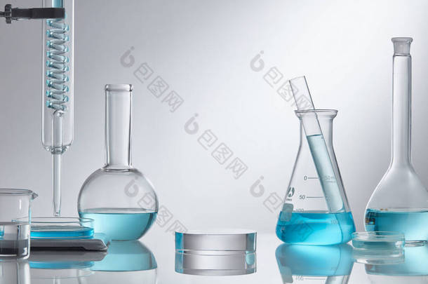 在实验室设备的现代玻璃基座上展示化妆品.实验室玻璃设备，白色底座上有蓝色水成份。研究与开发化妆品概念