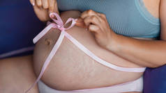 肚皮上缠着一条粉色带子的怀孕女孩的美女。美女怀孕特写。孕妇腹部皮肤的天然质感。皮肤上的拉伸痕迹，腹部皮肤受损