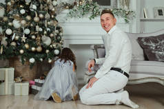 可爱的小女孩穿着蓝色衣服在圣诞客厅里和爸爸开心地玩着。圣诞时刻的概念，新年快乐，童年快乐。大气家庭时刻。复制空间