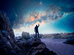 人站在岩石上，后视镜，举起一只手凝视着银河，星空掠过海洋