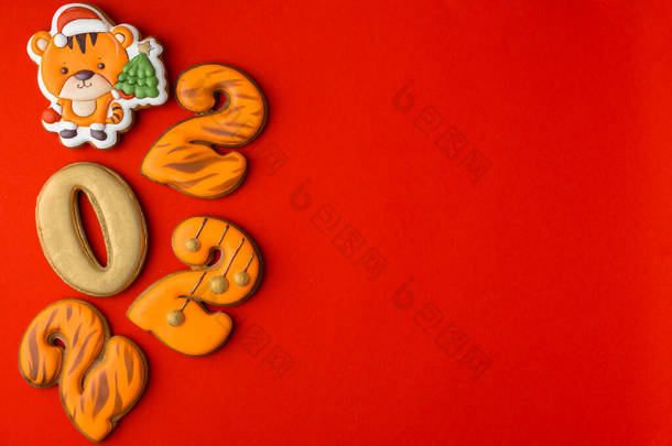 扁平的圣诞姜饼铺在红色的背景上，上面有橙色虎皮的糖霜。圣诞快乐，祝2022年新年快乐。虎年