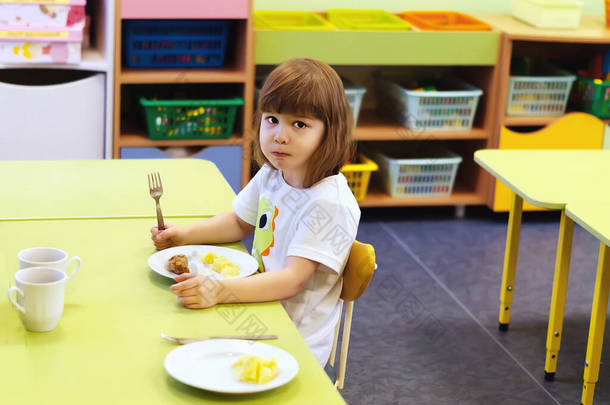 可爱的小女孩在<strong>幼儿园</strong>吃着<strong>健康</strong>的食物。一个漂亮的小女孩正坐在桌旁吃午饭。一个可爱的孩子在孩子们的教育中心吃着带有肉片的土豆.