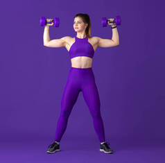 漂亮的年轻女运动员在紫色工作室背景，单色肖像上练习
