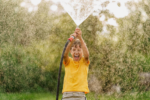 快乐的男孩在后院洒水，玩花园软管，在日落时洒水，喜欢在高温中洒水。儿童暑期娱乐和户外运动。有选择地把重点放在手头上.