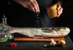 厨师准备新鲜的鱼、生鱼片、鲤鱼、撒盐.准备烹调鱼的食物。餐厅厨房的工作环境.
