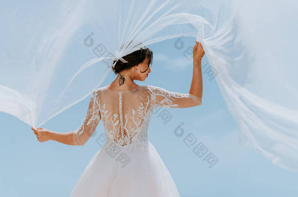 穿着白衣的浪漫美丽的新娘站在阳台上，背景是大海和群山