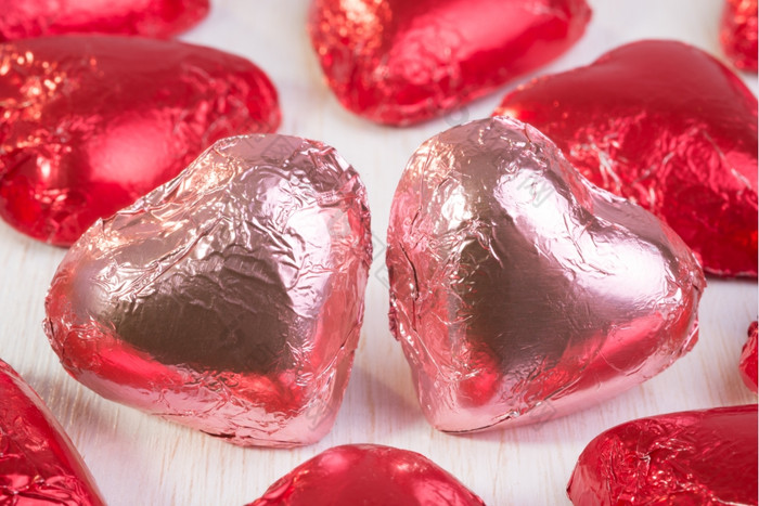 两个巧克力心粉红色的包装箔关闭在一起而且包围许多其他巧克力心红色的包装箔