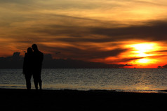 轮廓浪漫的度蜜月夫妇走的海滩与美丽的日出背景