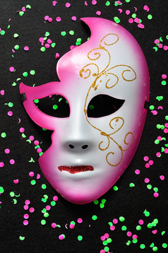 面具孤立的黑色的背景散落与粉红色的和绿色五彩纸屑