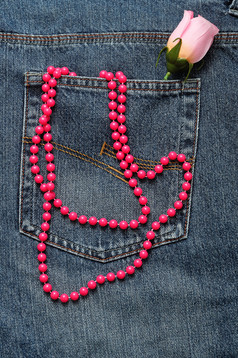 字符串粉红色的珠子和粉红色的人工玫瑰显示的回来口袋里牛仔布珍