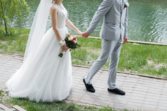 关闭时尚的新结婚了夫妇走在一起的公园背景湖他们的婚礼一天与花束