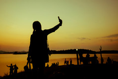 的轮廓女人拍摄自己在的人群附近的水的日落