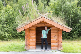 成人男人。等候为的公共汽车公共汽车站的一边的路的国家一边挪威传统的木公共汽车停止与草覆盖屋顶成人男人。等候为的公共汽车传统的公共汽车停止挪威