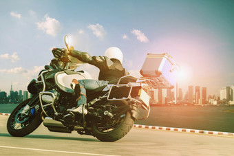 男人。骑巡回演出摩托车锋利的曲线为旅行和城市生活方式男人。骑巡回演出摩托车锋利的曲线对日落天空和高建筑小镇摩天大楼